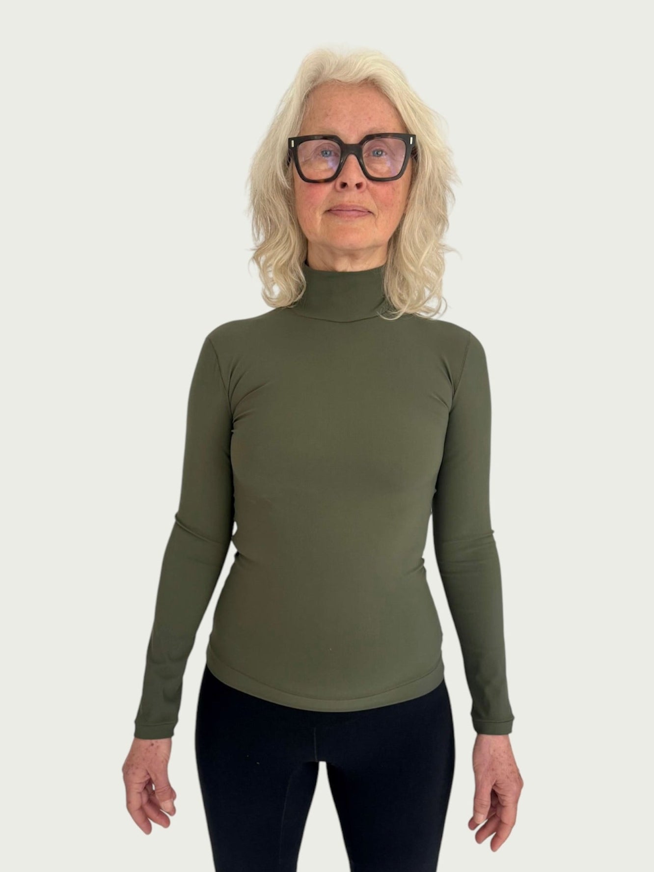 A person wearing a green mock neck longline top with slim sleeves and a hip length fit, paired with black trousers.