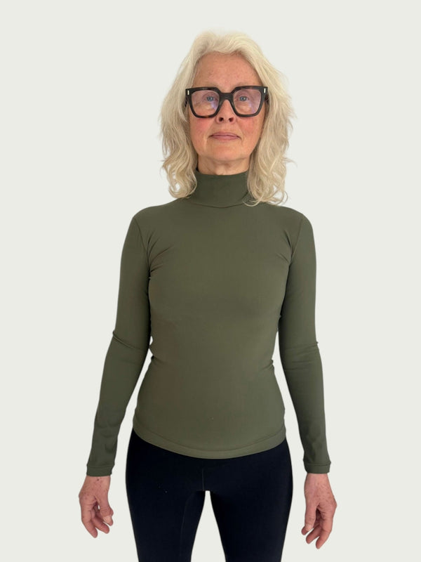 A person wearing a green mock neck longline top with slim sleeves and a hip length fit, paired with black trousers.