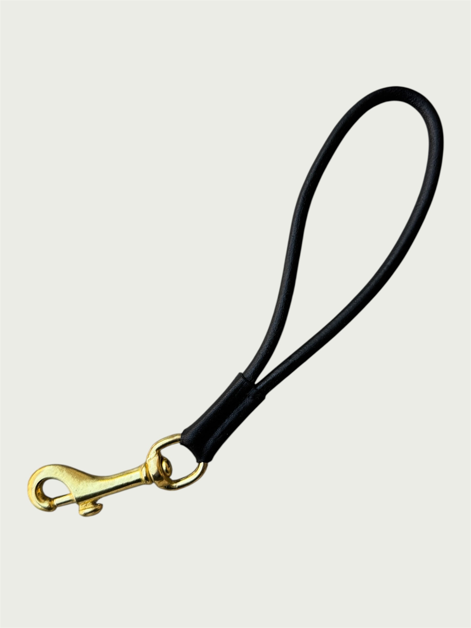 Flat lay of Wildgrain Leather Essential Loop Wrist Strap in Black with its handmade looped leather cord and solid brass hardware.