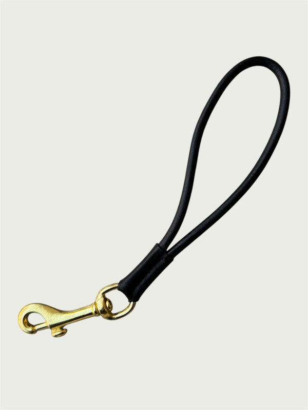 Flat lay of Wildgrain Leather Essential Loop Wrist Strap in Black with its handmade looped leather cord and solid brass hardware.