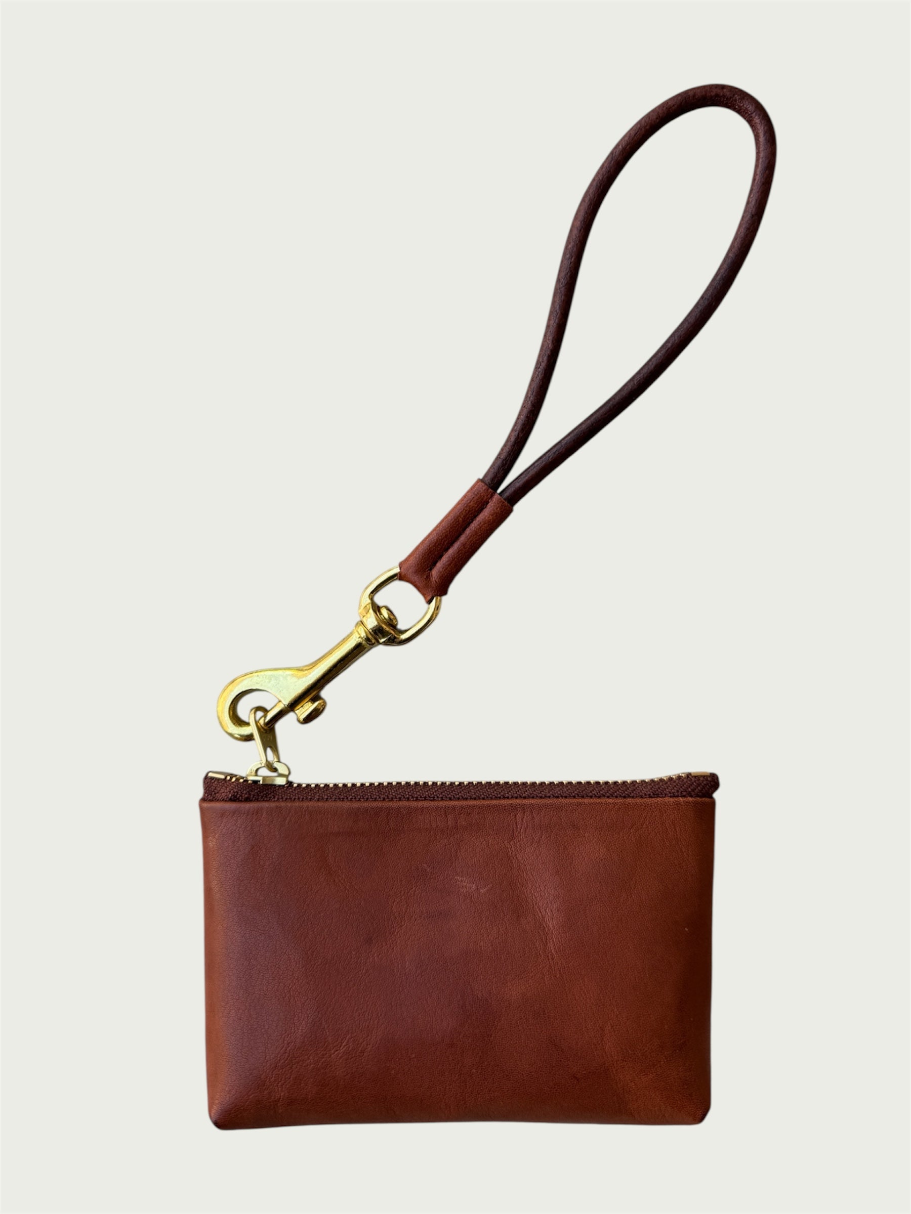 Flat lay of Wildgrain Essential Loop Wrist Strap in Cognac attached to zipper of Wildgrain Leather Mini Pouch in Cognac.