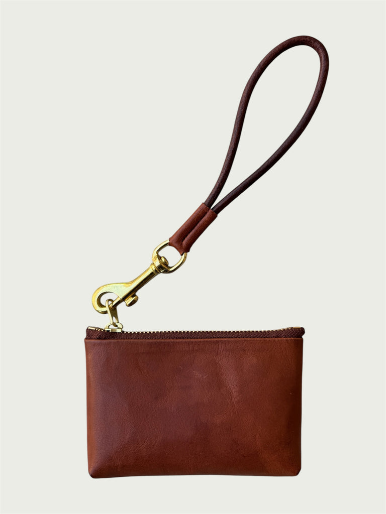 Flat lay of Wildgrain Essential Loop Wrist Strap in Cognac attached to zipper of Wildgrain Leather Mini Pouch in Cognac.