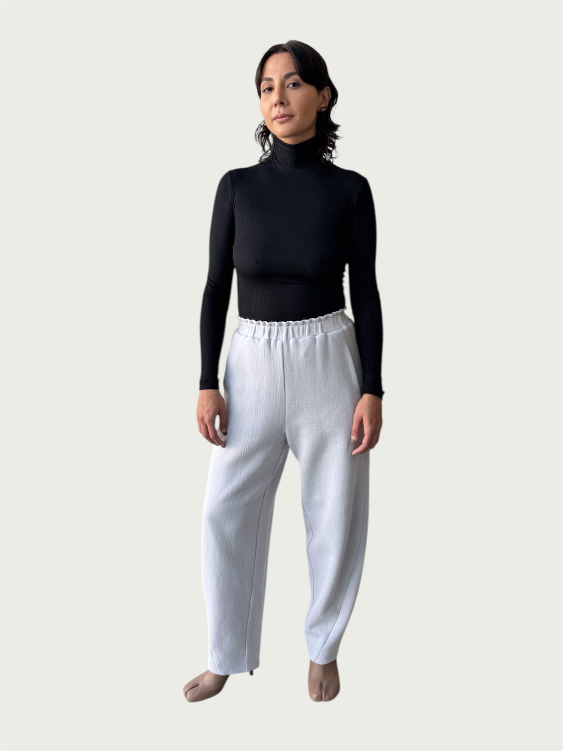 Model in Ribbed Mock Neck Shirttail Top in Black with long sleeves and a close, body-skimming fit, styled with the Organic Contoured Cotton Arc Pant in Porcelain.