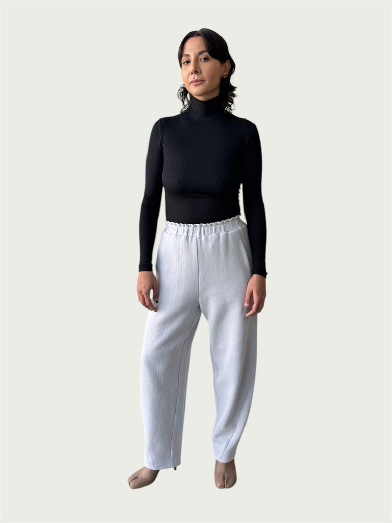 Model in Ribbed Mock Neck Shirttail Top in Black with long sleeves and a close, body-skimming fit, styled with the Organic Contoured Cotton Arc Pant in Porcelain.