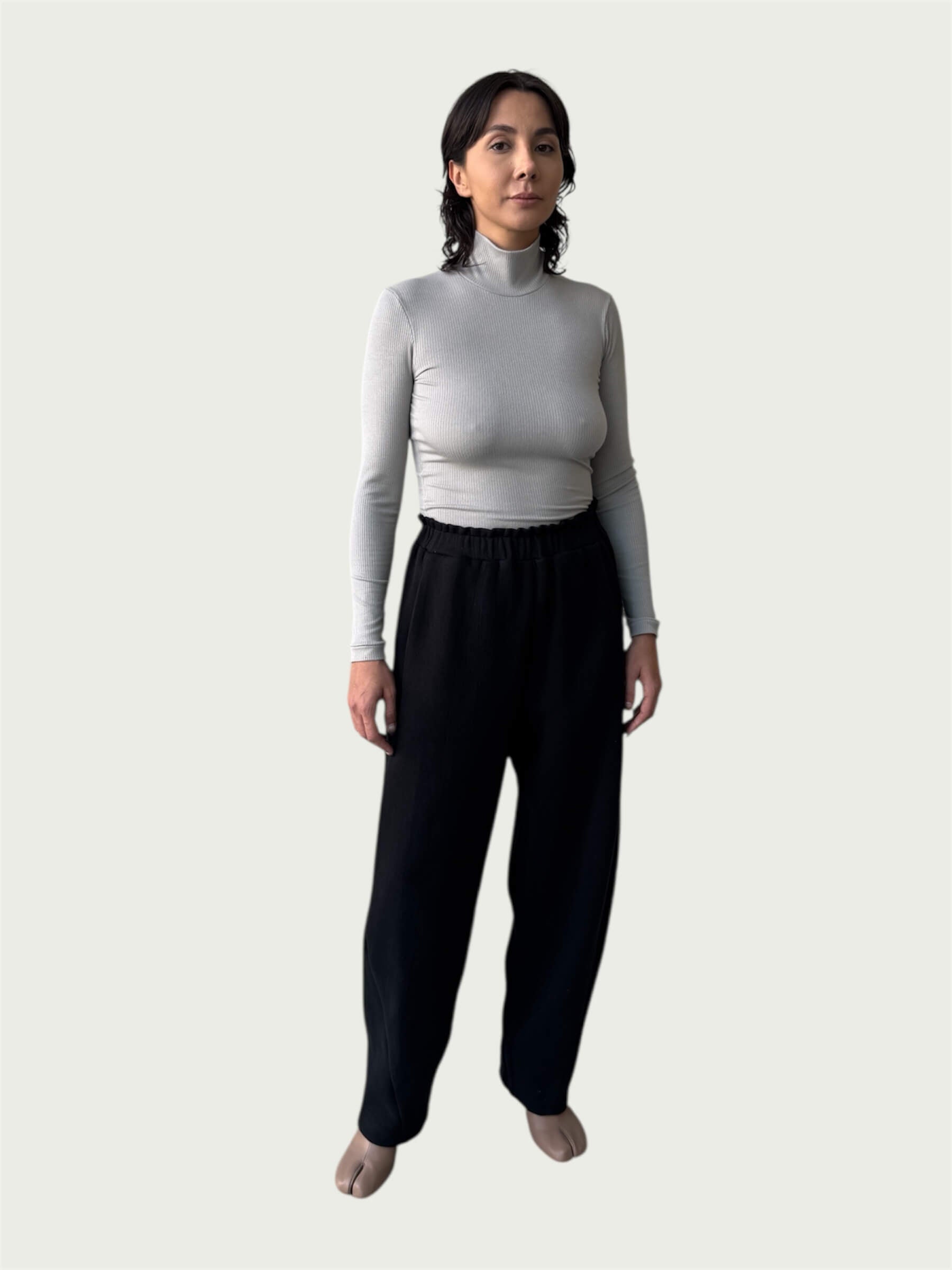 Model in Ribbed Mock Neck Shirttail Top in Dove Grey with long sleeves and a close, body-skimming fit, styled with the Organic Contoured Cotton Arc Pant in Black.