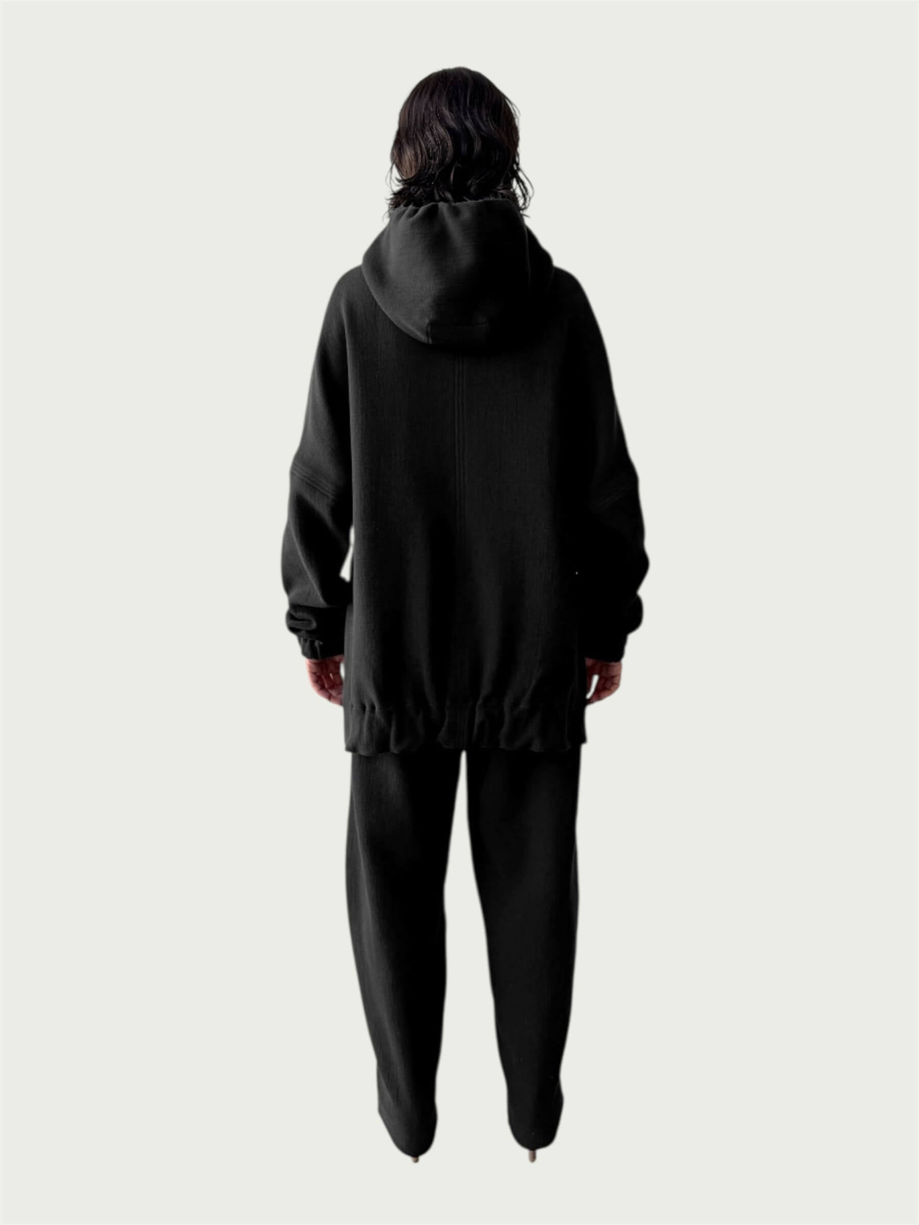 Rear view of model in Organic Contoured Cotton A.D.C. Hoodie in Black with gently gathered hem, falling below the hip; styled with Organic Contoured Cotton Arc Pant in Black.