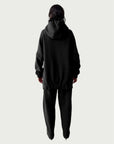 Rear view of model in Organic Contoured Cotton A.D.C. Hoodie in Black with gently gathered hem, falling below the hip; styled with Organic Contoured Cotton Arc Pant in Black.