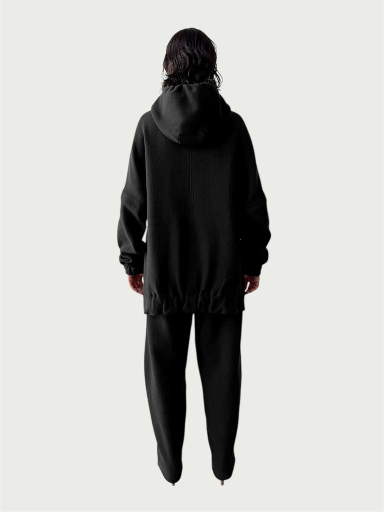Rear view of model in Organic Contoured Cotton A.D.C. Hoodie in Black with gently gathered hem, falling below the hip; styled with Organic Contoured Cotton Arc Pant in Black.