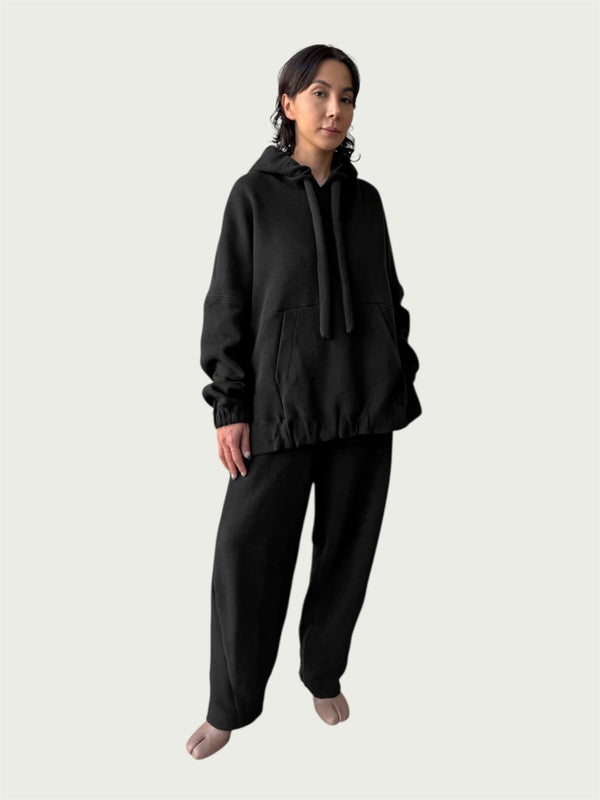 Model in the softly structured Organic Contoured Cotton A.D.C. Hoodie in Black that drapes with ease, styled with Organic Contoured Cotton Arc Pant in Black.