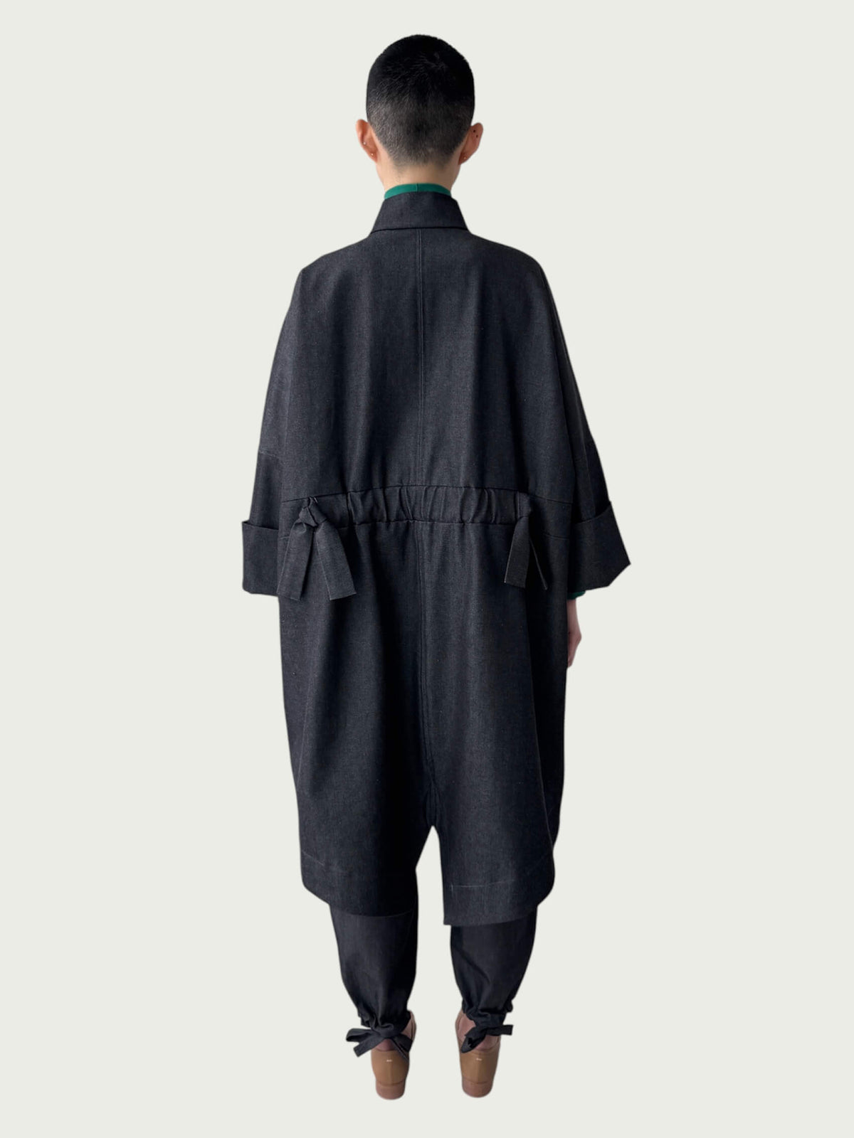Person wearing a black denim coat over coordinating denim pants on a white background