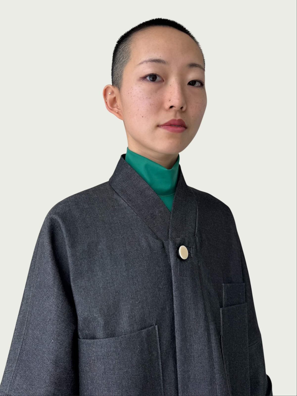 Person wearing a black denim coat over a green mock neck shirt on a plain background